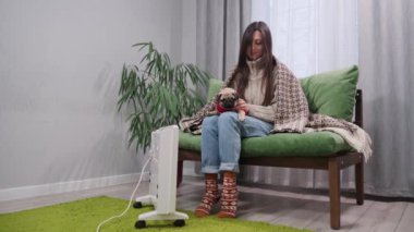 Sıcak giyimli genç bir dişi ve köpeği elektrikli radyatörün yanında ısınıyorlar..