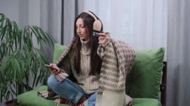 Genç bir kadın elektrik ve ısıtma faturalarını evdeki kanepede kredi kartıyla ödüyor..