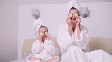 Anne ve kızı evde dinleniyor. Genç bir kadın ve dört yaşındaki kızı göz kapaklarında salatalık yüzükleriyle bir yatakta oturuyorlar..