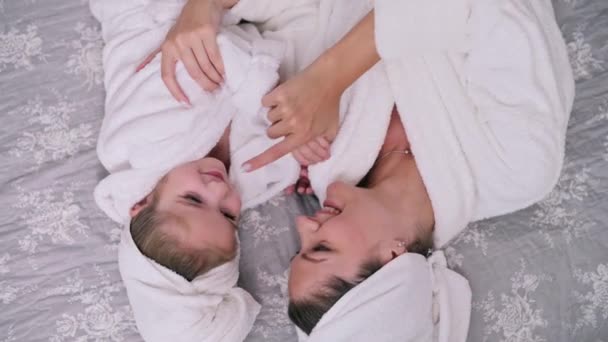 母と娘は家で休んでいる 若い女性と彼女の4歳の娘はベッドの上のバスローブに横たわっています — ストック動画