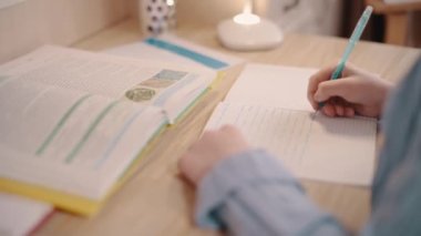 Ödev yapan bir kız. Kız odasındaki masada deftere yazıyor. Eller yukarı, seçici odaklanma.