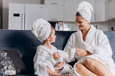 Genç bir anne ve anaokulu kızı evdeki kanepede fincanlardan çay içiyorlar..