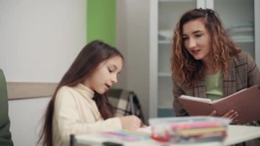 Kadın psikolog ofisteki bir kızla iletişim kuruyor. Çocuk çizer ve doktorla konuşur..