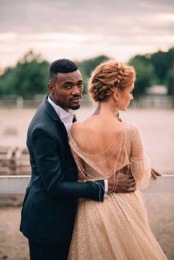 İki aşık, siyah erkek ve beyaz kadın gün batımında bir çiftlikte birbirlerine sarılıyorlar.