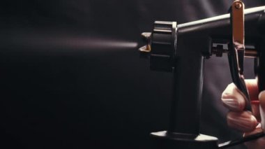 Cosmetologist using airbrush for spray tan in beauty salon. Close up of hand.