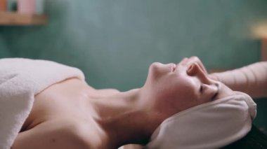 Genç ve çekici bir kadın spa 'da rahatça uzanıyor. Güzellik uzmanı yüz nemlendirici yapıyor..