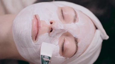 Kozmetik uzmanı müşterilerin yüzüne nemlendirici bir maske takıyor. Genç bir kadın kaplıcada rahat bir şekilde uzanıyor. Üst görünümü kapat.