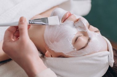 Kozmetik uzmanı müşterilerin yüzüne nemlendirici bir maske takıyor. Genç bir kadın kaplıcada rahat bir şekilde uzanıyor. Kapat..