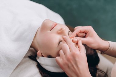 Güzellik uzmanı genç bir kadına derin bir yüz masajı yapıyor. Yaşlanmaya karşı yüz masajı tekniği. Yakın plan..