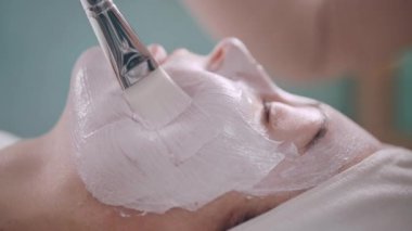 Kozmetik uzmanı müşterilerin yüzüne nemlendirici bir maske takıyor. Genç bir kadın kaplıcada rahat bir şekilde uzanıyor. Kapat..
