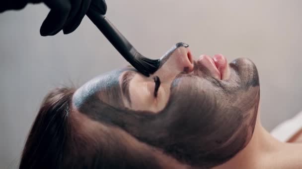 きれいな女性の顔に黒いマスクを適用する美容室 顔の手続きを持つスパの女性 — ストック動画