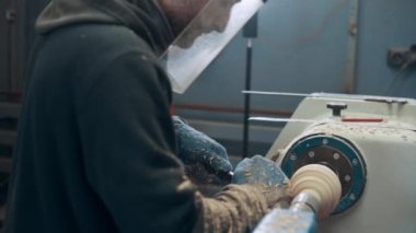 Marangoz torna tezgahına bir parça mobilya kazıdı. Koruyucu maskeli bir adam fabrikada çalışıyor..