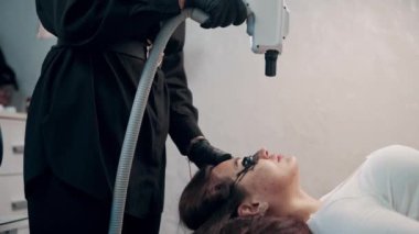 Uzman kozmetolojist salonda lazer kullanarak karbon soyma işlemi yapıyor. Sabit çekim.