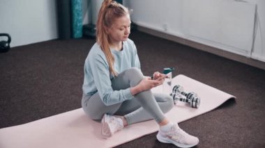 Genç atletik kadın spor salonunda dinlenirken akıllı telefon kullanıyor. Eğitim için mobil uygulama.