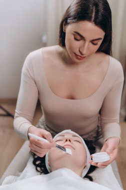 Kozmetik uzmanı müşterilerin yüzüne nemlendirici bir maske takıyor. Genç bir kadın kaplıcada rahat bir şekilde yatıyor..