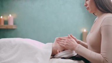 Güzellik uzmanı yüz masajı yapıyor. Genç bir kadın sırt üstü uzanıyor ve kaplıca salonunda yüzünü gerdiriyor. Yaşlanmaya karşı masaj teknikleri.