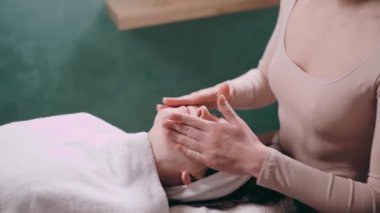 Güzellik uzmanı yüz masajı yapıyor. Genç bir kadın sırt üstü uzanıyor ve kaplıca salonunda yüzünü gerdiriyor. Yaşlanmaya karşı masaj teknikleri.