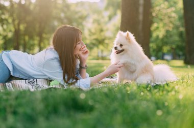 Parkta sevimli köpeği olan genç bir kadın. Pomeranian Spitz ve sahibi çimlerin üzerinde oturuyorlar..