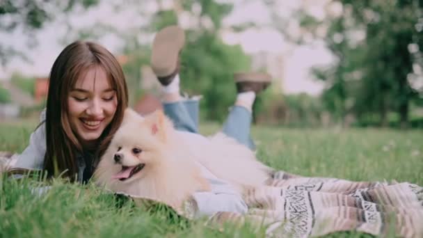 公園でかわいい犬を飼っている若い女性 所有者と一緒にポメラニアン スピッツは草の上に座っている — ストック動画