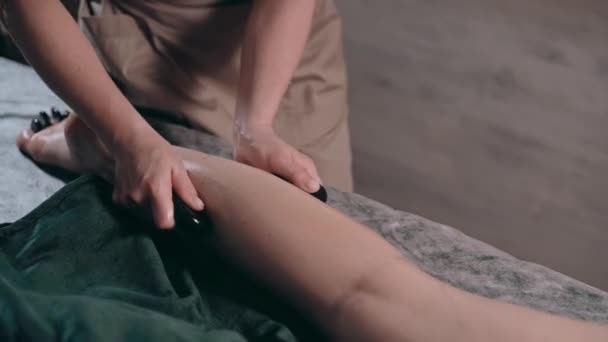 スパサロンで脚やタトゥーのためにホットストーンマッサージをしている若い女性 クローズアップ — ストック動画