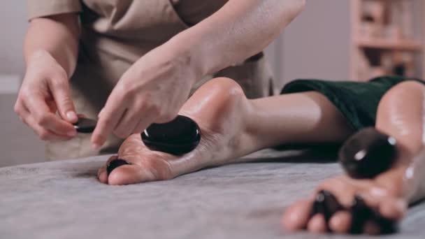 温泉サロンで足のための熱い石のマッサージを持っている若い女性 — ストック動画