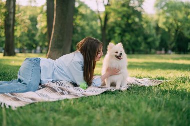 Parkta sevimli köpeği olan genç bir kadın. Pomeranian Spitz ve sahibi çimlerin üzerinde oturuyorlar..