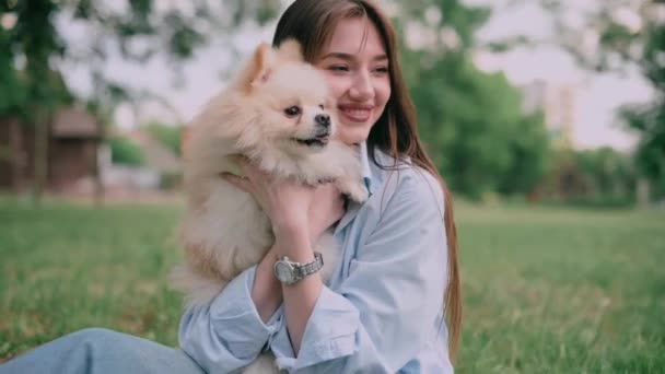 公園でかわいい犬を飼っている若い女性 所有者と一緒にポメラニアン スピッツは草の上に座っている — ストック動画
