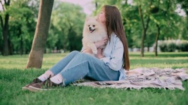 Parkta sevimli köpeği olan genç bir kadın. Pomeranian Spitz ve sahibi çimlerin üzerinde oturuyorlar..