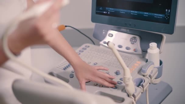 若い女性医師が診療所で超音波マシンを調整しています コントロールパネルのクローズアップ — ストック動画