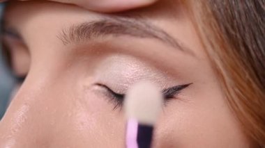 Profesyonel makyaj. Makyaj sanatçısı gölgeyi bir fırçayla göz kapağına uyguluyor. Aşırı yakın çekim.