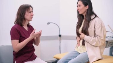 Genç bir kadın klinikteki karın ağrısı hakkında jinekoloğa şikayette bulunuyor. Doktor klinikteki bir hastaya danışıyor..