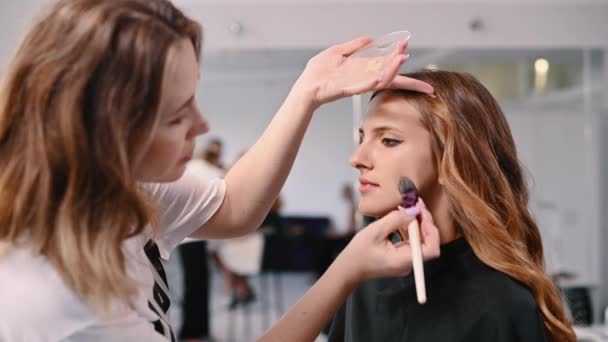 化妆师在沙龙用刷子把粉底刷在一位年轻女子的脸上 — 图库视频影像