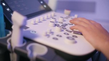 Genç bir kadın doktor klinikteki ultrason cihazını ayarlıyor. Kontrol panelinin kapanışı.