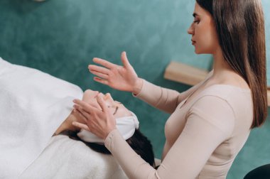 Güzellik uzmanı yüz masajı yapıyor. Genç bir kadın sırt üstü uzanıyor ve kaplıca salonunda yüzünü gerdiriyor. Yaşlanmaya karşı masaj teknikleri.