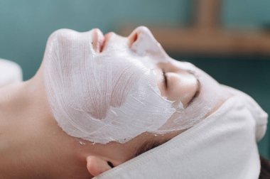 Nemlendirici yüz maskesi. Genç bir kadın kaplıcada rahat bir şekilde uzanıyor. Yüzünü kapat..