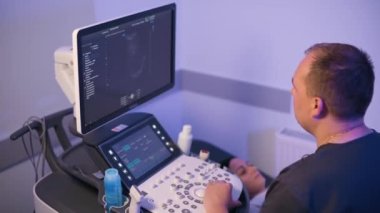 Erkek bir doktor, klinikteki bir hastaya ultrason uygular. Terapist dikkatlice cihazın ekranına bakar..
