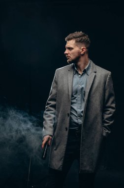 Dedektif bölgeyi inceliyor. Elinde fenerle karanlıkta duran ceketli, ciddi bir genç adam..