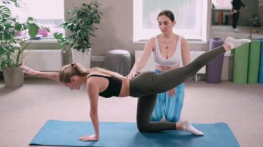 Spor salonunda pilates yapan iki genç atletik kadın. Eğitmen, müşterinin egzersizi yapmasına yardım eder.