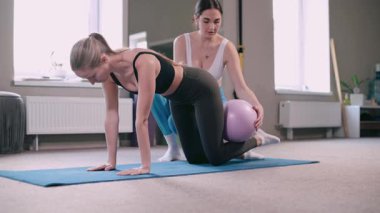 Pilates yapan kadınlar. Antrenör, müşterinin jimnastik topuyla egzersiz yapmasına yardım eder..