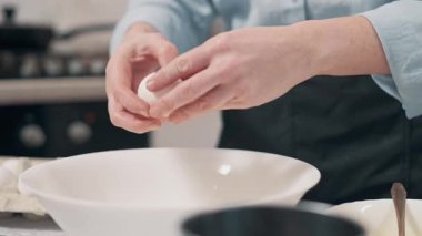 Yemek hazırlayan kadın. Kadın mutfakta cam kaseye yumurta kırıyor. Ellerin yakın çekimi.