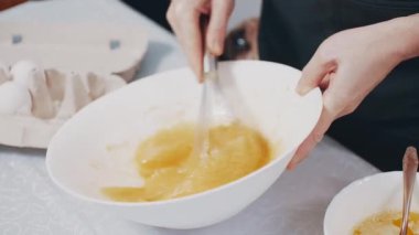 Kadın ev yemeği hazırlıyor. Kadın, evdeki mutfakta bir kasede yumurta çırpıyor. Yakın plan..