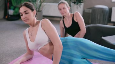 Spor salonunda pilates yapan iki genç atletik kadın. Eğitmen egzersizin doğru uygulandığını gösterir.
