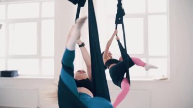 İnce vücutlu iki kız spor salonunda esnek kumaş üzerinde egzersiz yapıyor. Yavaş çekim.