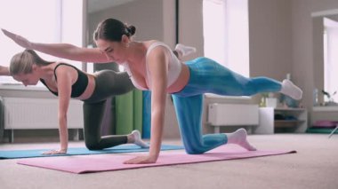 Spor salonunda pilates yapan iki genç atletik kadın. Eğitmen egzersizin doğru uygulandığını gösterir.