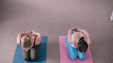 Spor salonunda pilates yapan iki genç atletik kadın. Antrenör egzersizin doğru uygulandığını gösteriyor. Üst görünüm.