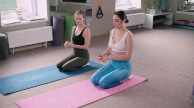 Spor salonunda pilates yapan iki genç atletik kadın. Eğitmen egzersizin doğru uygulandığını gösterir.