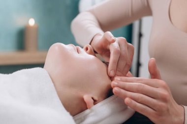 Güzellik uzmanı genç bir kadına derin bir yüz masajı yapıyor. Yaşlanmaya karşı yüz masajı tekniği. Yakın plan..