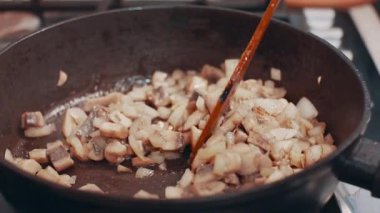 Bir aşçı kızartma tavasında mantar kızartır ve ahşap bir spatulayla karıştırır. Yakın plan..