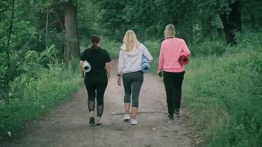 Üç orta yaşlı kadın spor yapmak için parka gider. Arka görünüm.
