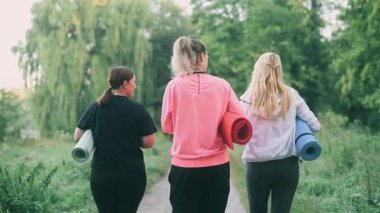 Üç orta yaşlı kadın spor yapmak için parka gider. Arka görünüm.
